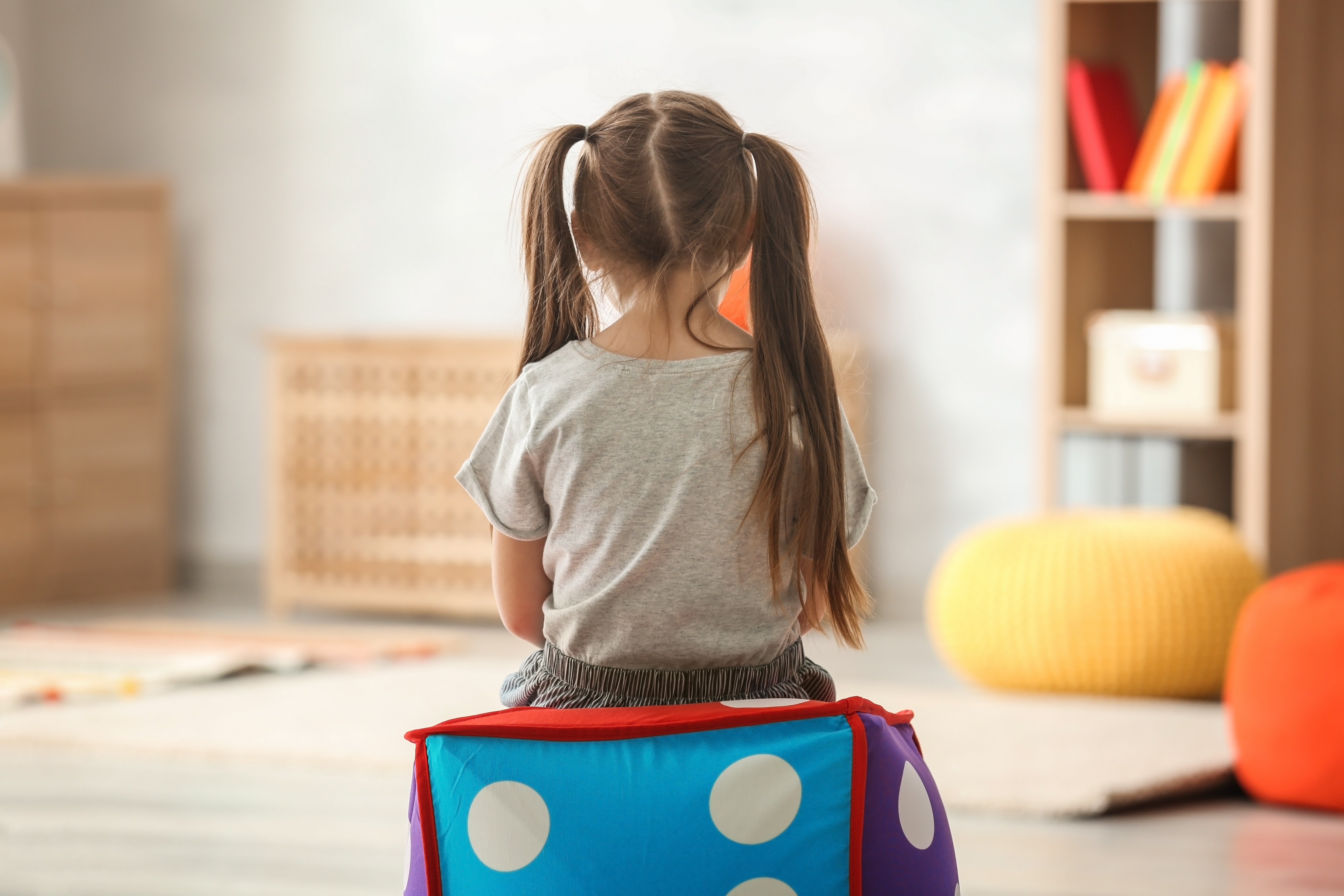 A child, facing away from the camera, sits on a colorful ottoman