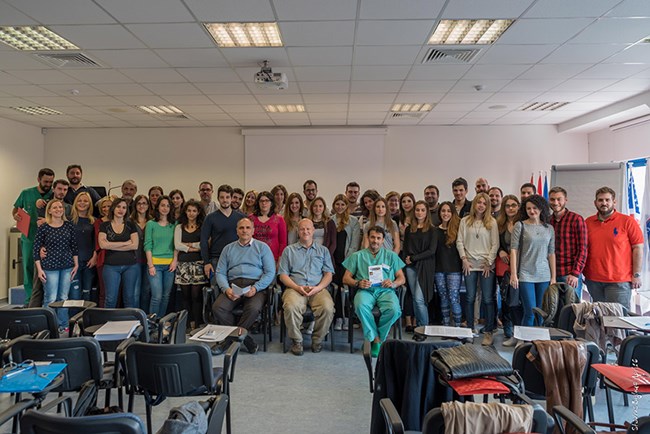 A large group of people poses for a photo in a classroom-like setting
