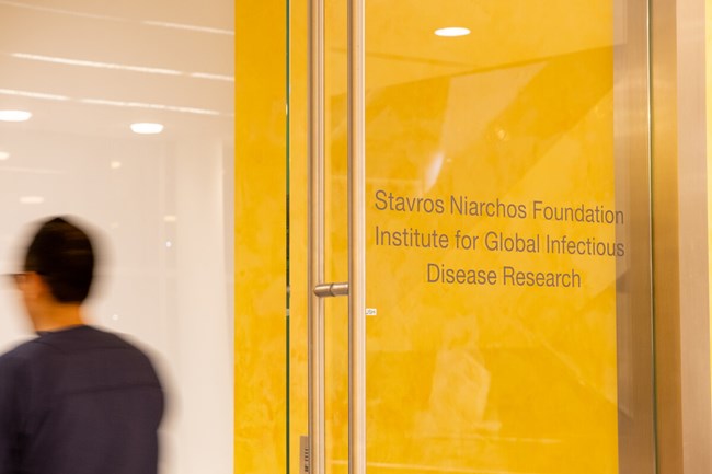 Μια γυάλινη πόρτα μπροστά από έναν κίτρινο τοίχο  που γράφει "Stavros Niarchos Foundation Institute for Global Infectious Disease Research"