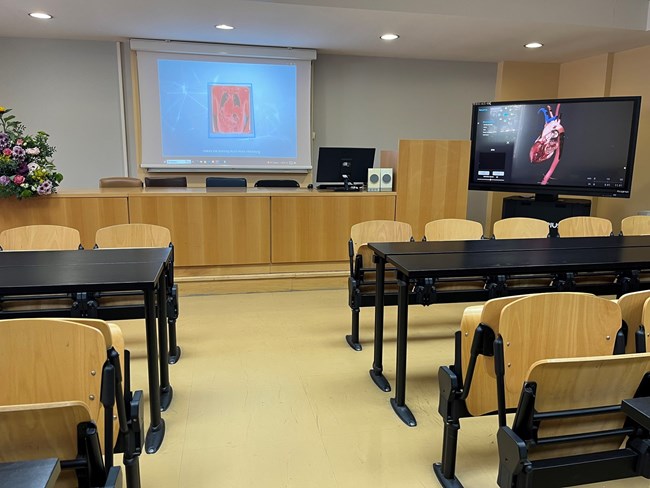 A classroom with chairs and a projector screen for presentations and the anatomage table.