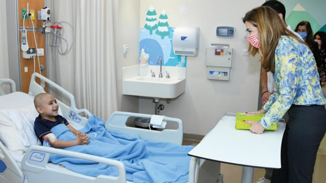 A child in a hospital bed smiles at adults at the foot of their bed