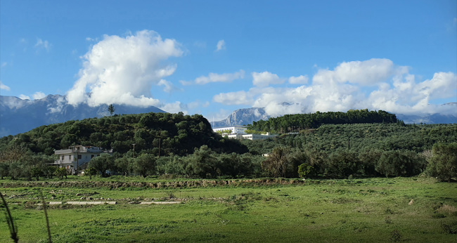 Μια απεικόνιση του κτιρίου του Γενικού Νοσοκομείου Σπάρτης ΙΣΝ  στην κορυφή ενός λόφου με καταπράσινο τοπίο 