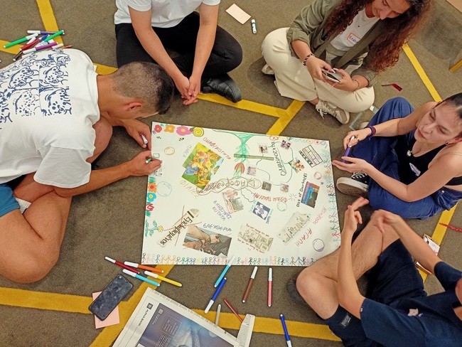 Seated young people use markers to create a colorful poster